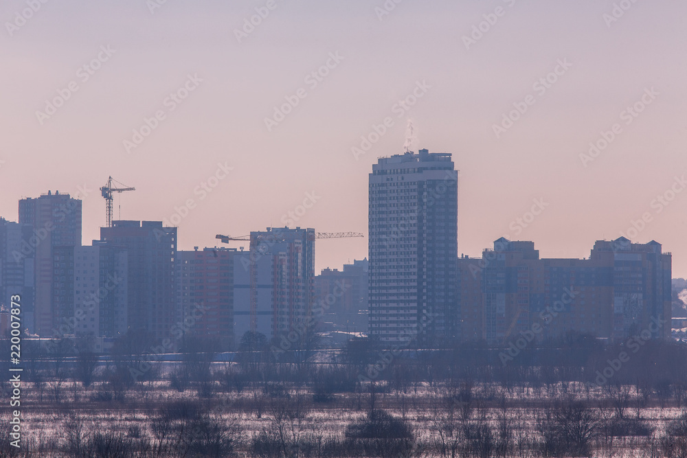 Winter landscape industrial outskirts of the city. Silhouettes of buildings and cranes.