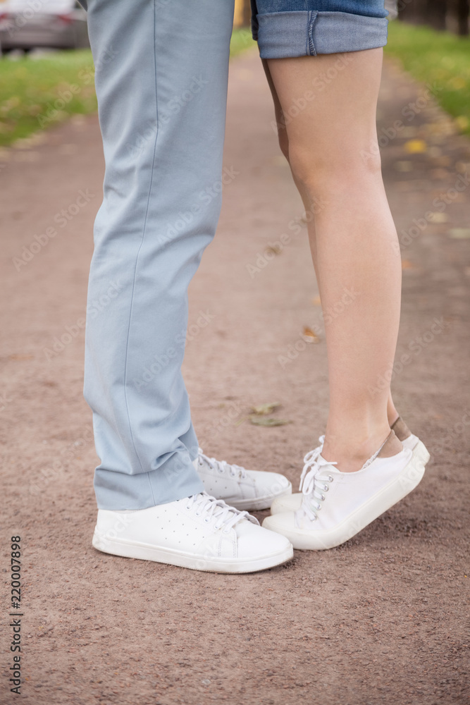 Close up of loving girlfriend standing tiptoe trying to hug boyfriend outdoors in park, romantic millennial couple in jeans and white sneakers embracing on street, small woman reach husband to kiss