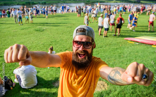 Urban event celebration. Cheerful fan at summer fest. Man bearded hipster in front of crowd people raise fists green riverside background. Hipster in cap happy celebrate event picnic fest or festival photo