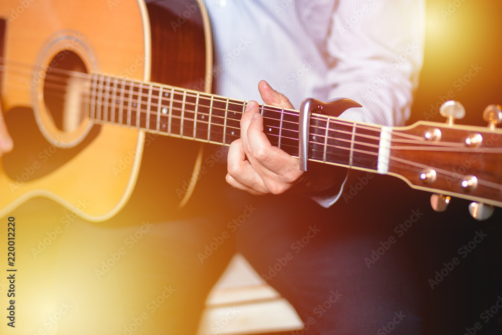 Fototapeta premium Guitar with a man's male hands playing the guitar on wooden wall background, electric or acoustic guitar with nature light. Concept of guys boys band performing on events 