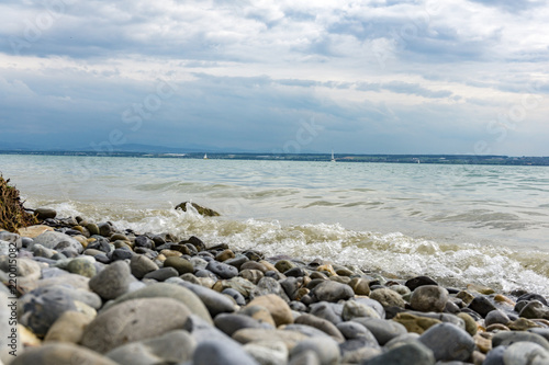 Strandufer mit bunten Steinen am Bodensee. Sommertag am Bodensee mit Mini Wellen.