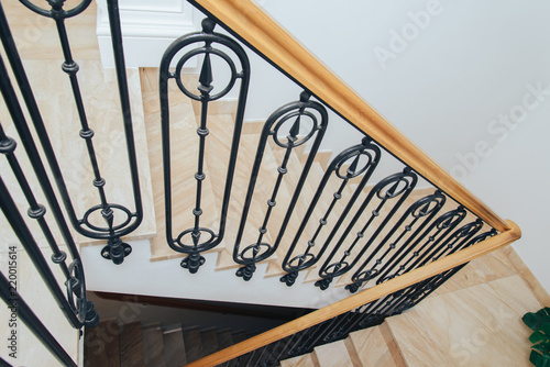Spiral staircase with wooden railing, marble steps and wrought iron balusters, top view.