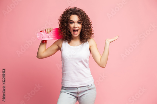 Portrait of funny hipster girl with pink longboard over pink background.