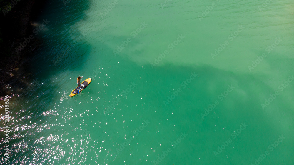 Fototapeta premium vue aérienne sur une personne debout sur un stand up paddle jaune sur des eaux vertes 