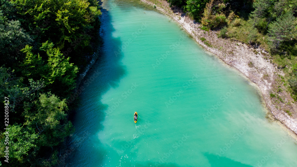 vue aérienne sur un lac aux eaux vertes émeraudes avec une personne sur un stand up paddle