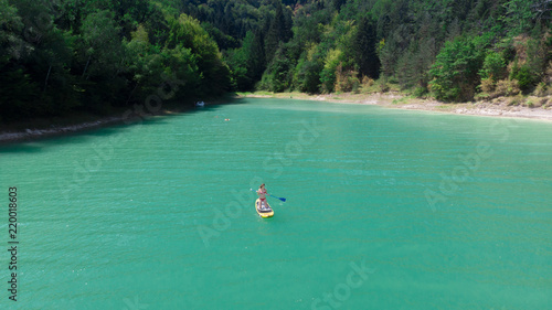 une jeune fille à genou sur son stand up paddle jaune, au milieu d'une eau verte