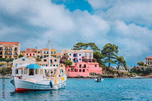 View of beautiful bay of Assos village with fishing boat at anchor in front and clouds in background, Kefalonia island, Greece