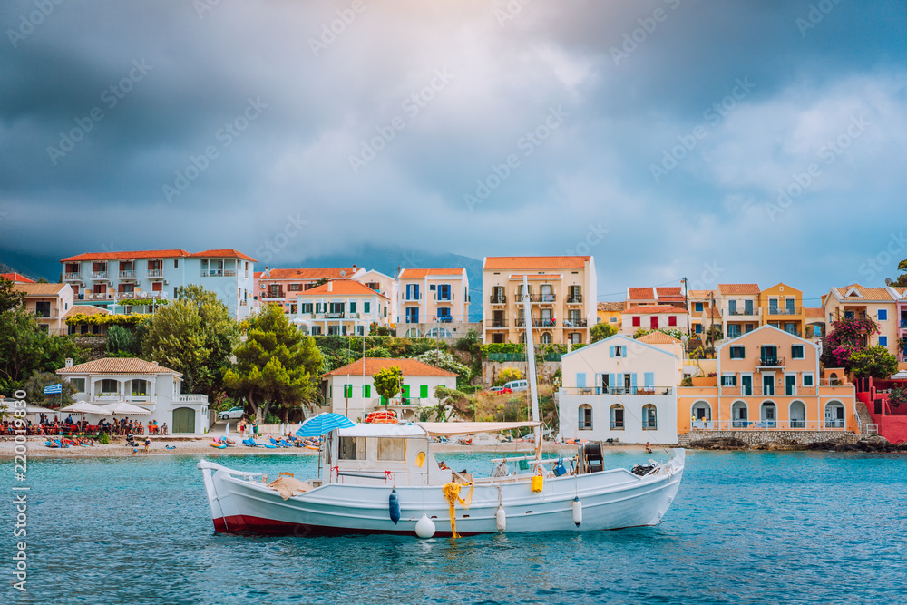 Unique majestic bay of Assos village with fishing boat at anchor in front and clouds in background, Kefalonia island, Greece