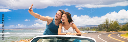 car road trip vacation young people taking selfie photo with phone during summer travel vacation. Tourists couple taking photos on Hawaii in convertible car, with smartphone camera. Banner panorama.