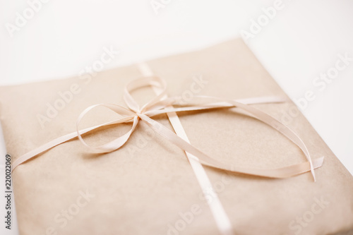 Cardboard carton package wrapped with light brown paper and tied with pink string ribbon in bow. Craft paper texture on white background. Gift present holiday birthday concept.
