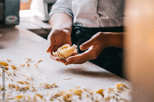 Chef woman's hands making tagliatelle pasta. Cooking process. Raw food photography concept.