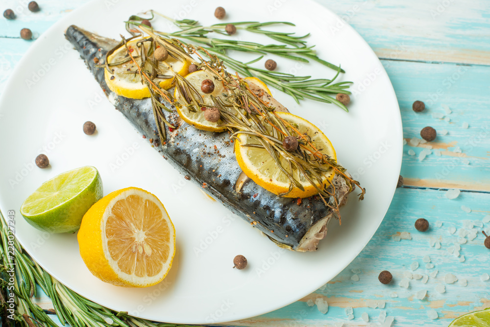 Cooked mackerel on a white plate with spices, herbs, lemon, lime and salt. A large plan