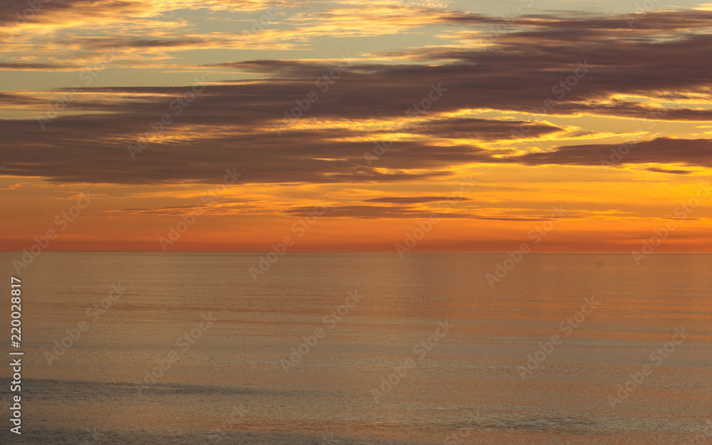Golden sunset colors of orange, gold, blue clouds reflected in calm ocean