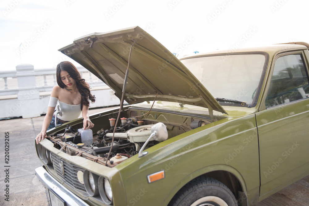 Adult woman repairing car. Woman on a roadtrip having a problem with her old car. Women spection She opened the hood Broken car on the side See engines that are damaged or not.
