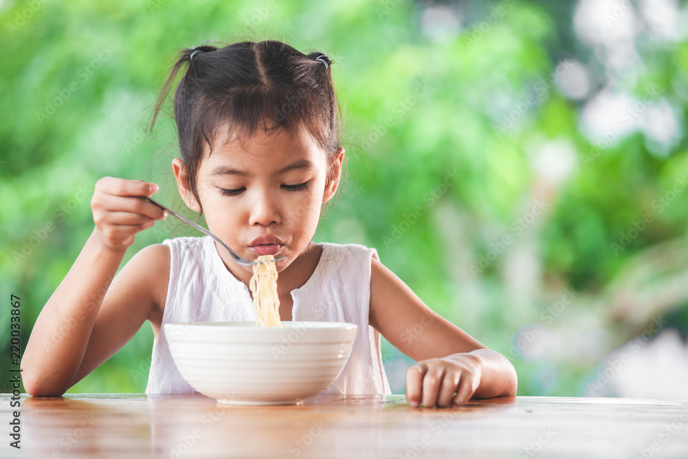 Cute asian child girl eating delicious instant noodles with fork in the nature background Cute asian child girl eating delicious instant noodles with fork in the nature background