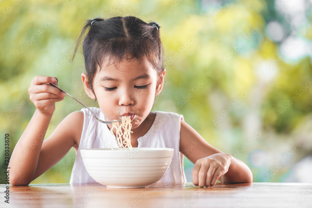 Cute asian child girl eating delicious instant noodles with fork in the nature background Stock