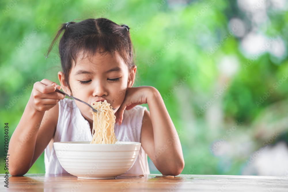 Cute asian child girl eating delicious instant noodles with fork in the nature background Cute asian child girl eating delicious instant noodles with fork in the nature background