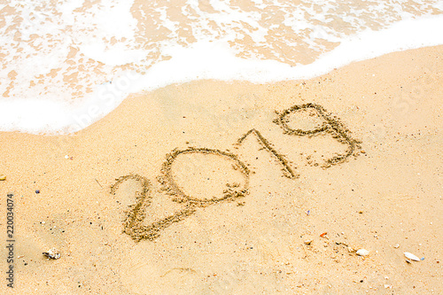 Year 2019 written at the sand beach with sea wave water. wave coming to 2019 concept on the sand beach in the morning.Text 2019 on a beach sand. Concept New Year 2019 is coming soon