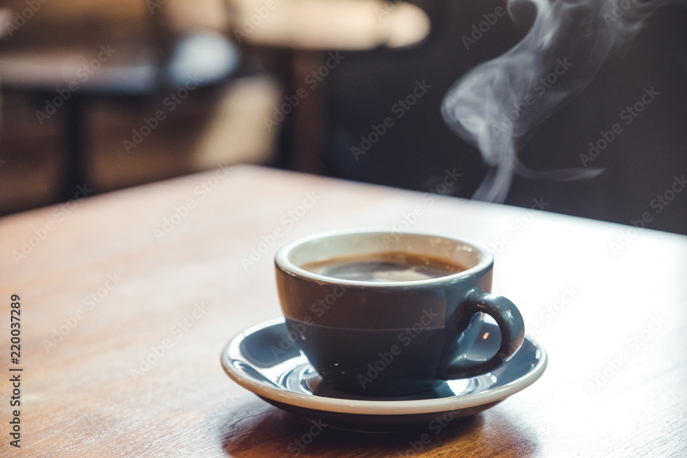 Fototapeta Closeup image of a blue cups of hot coffee with smoke on vintage wooden table in cafe