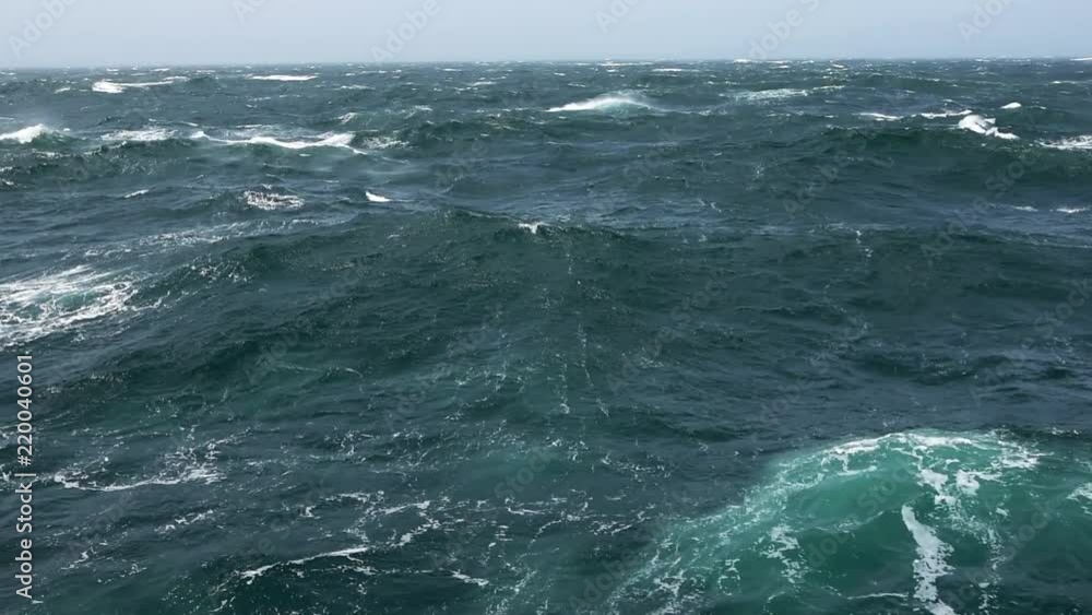 Cargo ship rolling in stormy sea. Huge waves under blue sky in Indian Ocean