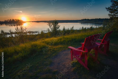 A beautiful summer sunset over a lake with with red chairs photo
