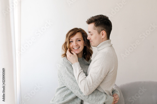 Embracing man and woman in sweaters standing in embracing at home being in love