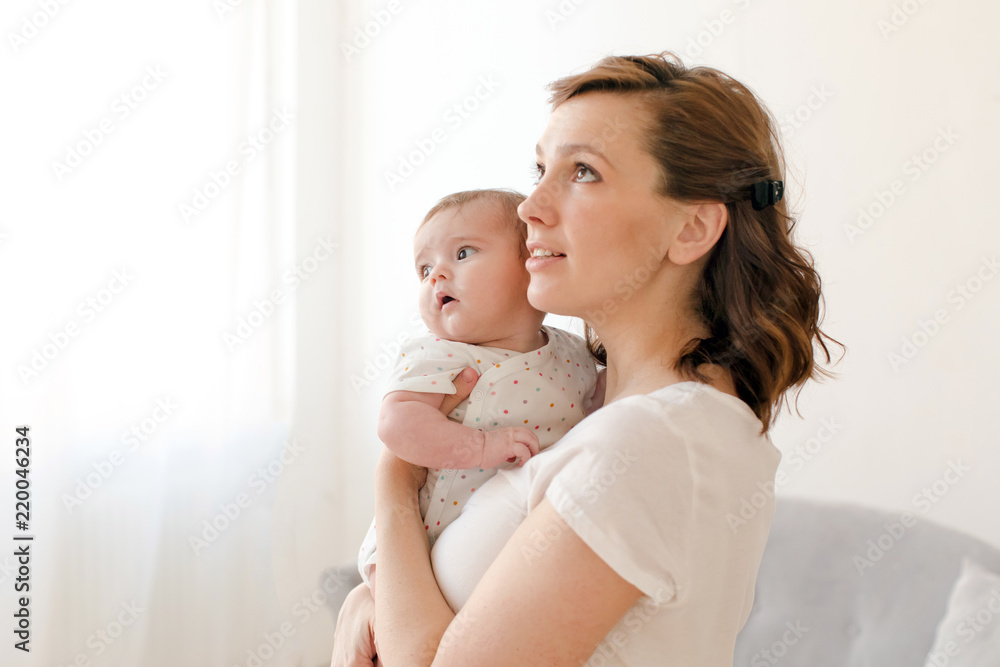 Beautiful young woman with baby on hands looking up while standing at home Beautiful young woman with baby on hands looking up while standing at home