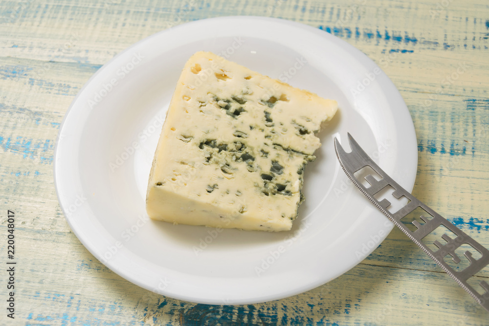 A piece of blue cheese on a plate with a cheese knife on a wooden background.