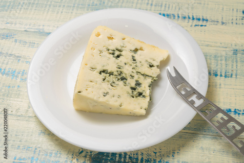 A piece of blue cheese on a plate with a cheese knife on a wooden background.