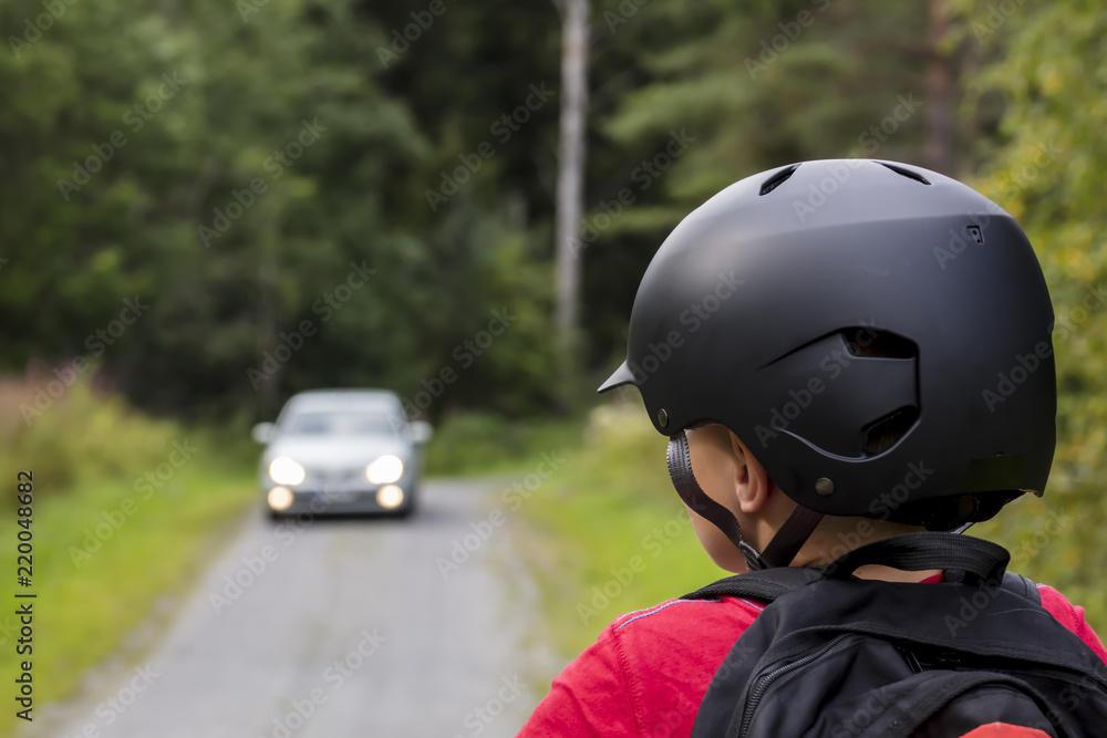 An unidentified little boy looks at the car that is coming in Finland. He has a black bicycle helmet on his head. In the back he has a backpack. An unidentified little boy looks at the car that is coming in Finland. He has a black bicycle helmet on his head. In the back he has a backpack.