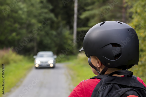 An unidentified little boy looks at the car that is coming in Finland. He has a black bicycle helmet on his head. In the back he has a backpack. © Jarkko