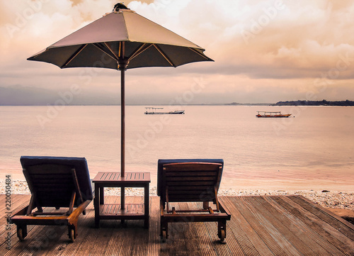Two sunbeds and umbrella standing on a wooden platform on the tropical beach at sunset. Concept of calm rest 