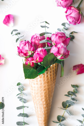 Still life of a bouquet of pink roses and eucalyptus inside a waffle cone on white background. The concept of gift and celebration. Flat lay, top view.