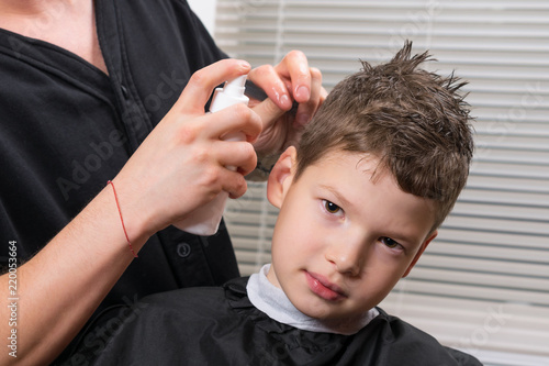 the hairdresser moistens the boy's hair with a sprayer to do the haircut