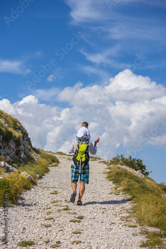 Father and son walking along the mountain road disappearing in the cloudy sky. Travel adventure and hiking activity with child, active and healthy lifestyle.