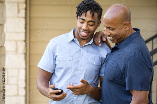 African American father and his adult son texting.