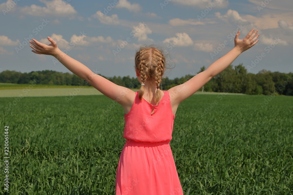 Young girl / teenager, woman enjoy life, stands on her back in green field, with hands up, blond hair, in summer pinbk sleeveless dress, blue sky with few clouds Young girl / teenager, woman enjoy life, stands on her back in green field, with hands up, blond hair, in summer pinbk sleeveless dress, blue sky with few clouds