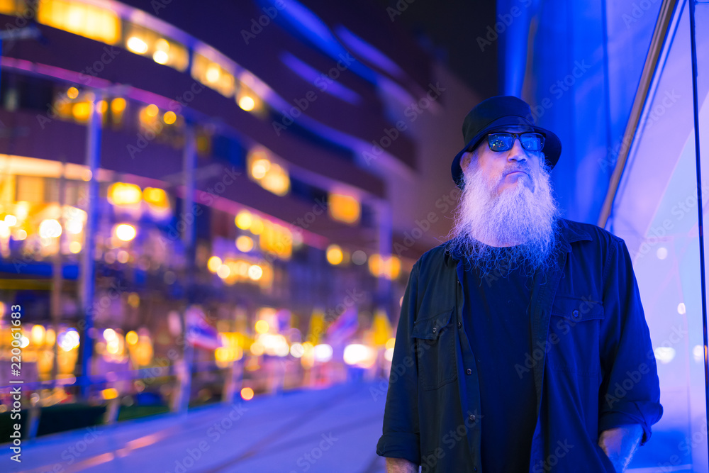 Mature bearded tourist man against blue light in the city streets at night