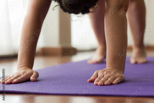 Hands and feet of woman on purple yoga mat while performing downward facing dog. Female yogi beginner practices adho mukha svanasana pose. Focus, concentration, healthy lifestyle concepts