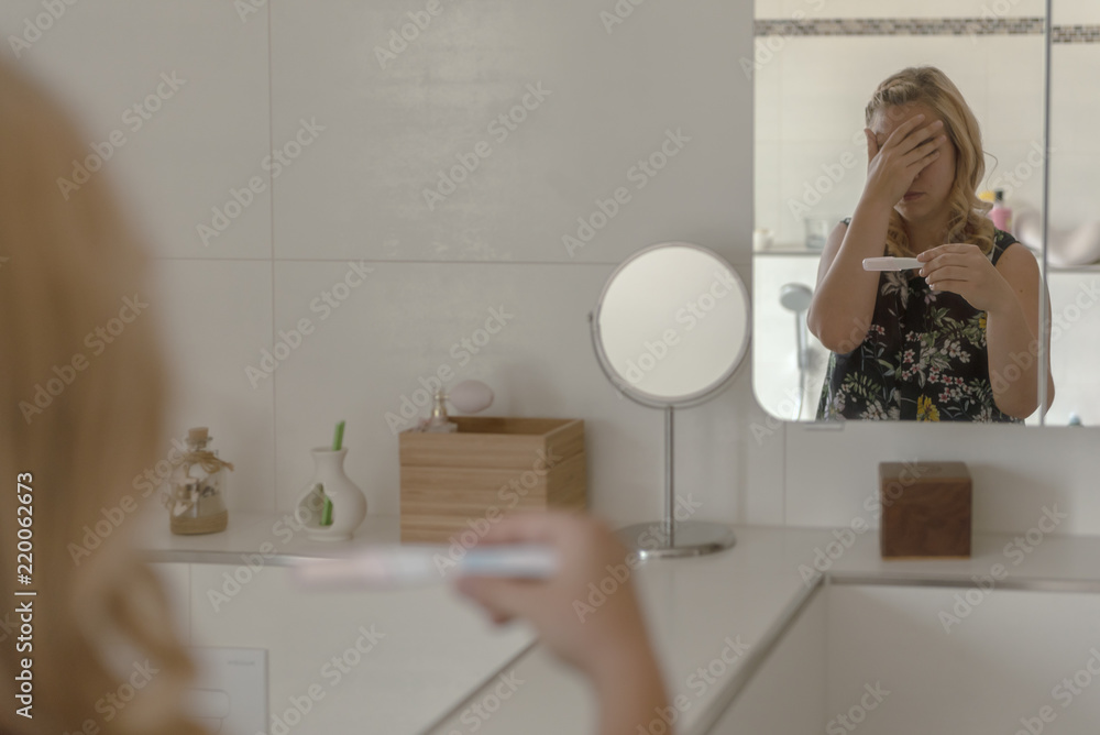 A woman controls a pregnancy test and is shocked by the result. Concept: health and hygiene A woman controls a pregnancy test and is shocked by the result. Concept: health and hygiene