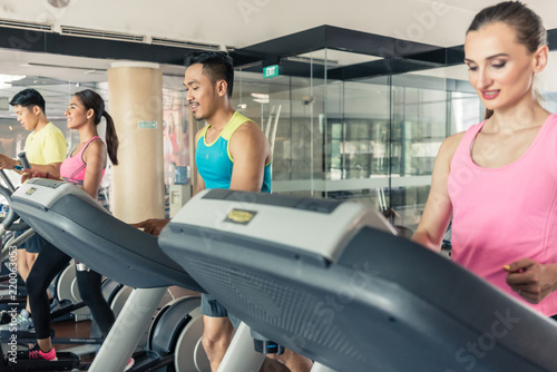 Full length rear view of a fit active woman running on treadmill during workout session in a trendy fitness club with modern equipment
