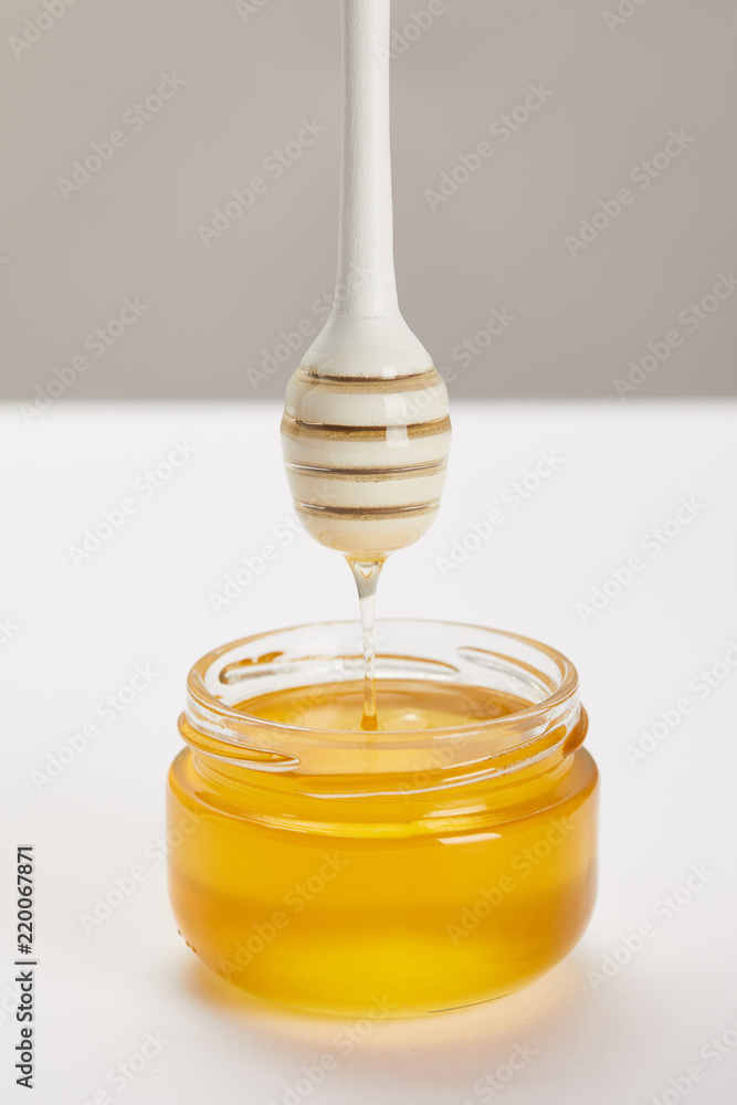 close up view of wooden honey deeper with organic honey and glass jar on grey background close up view of wooden honey deeper with organic honey and glass jar on grey background