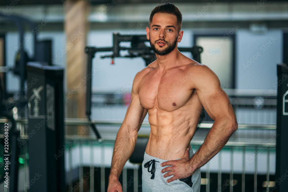 Young athlete posing with a torso for photography on a gym background. Bodybuilder, athlete with pumped muscles Young athlete posing with a torso for photography on a gym background. Bodybuilder, athlete with pumped muscles