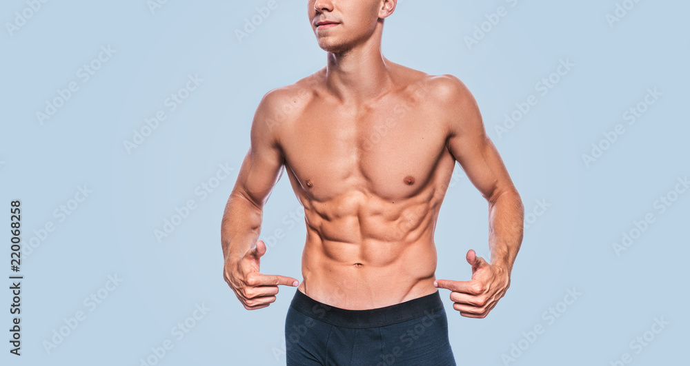 Horizontal studio image of fitness muscular male model in black underwear showing his abdominal press on a blue background. Cropped head portrait of sporty healthy strong athletic man with sexy torso.