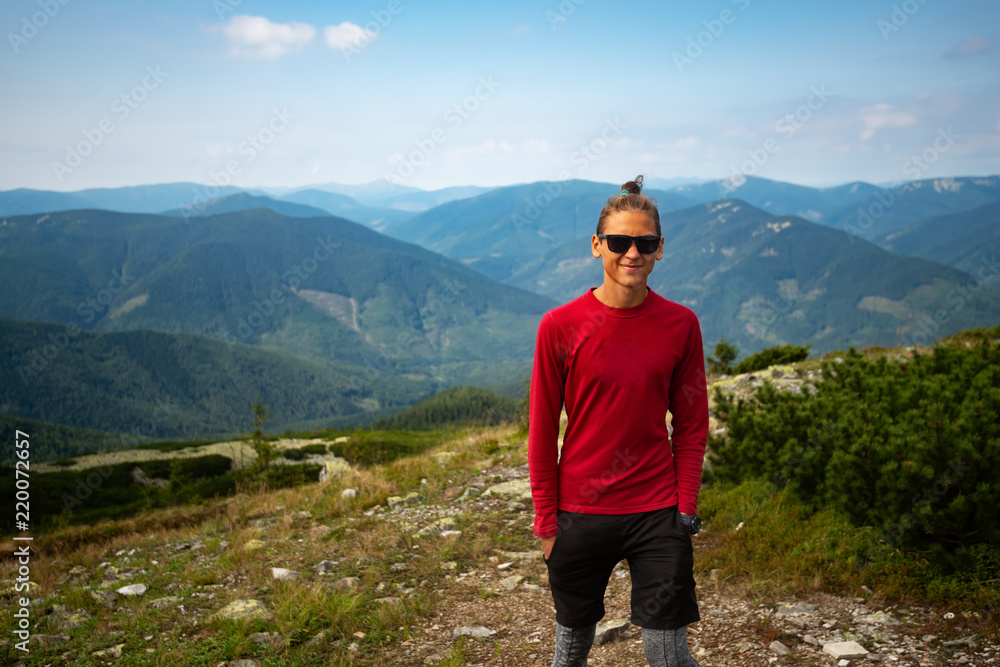 Joyful adventurer, guy teenager stands in the mountains