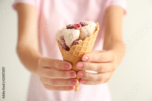 Woman holding waffle cone with delicious ice cream and raspberries on light background  closeup