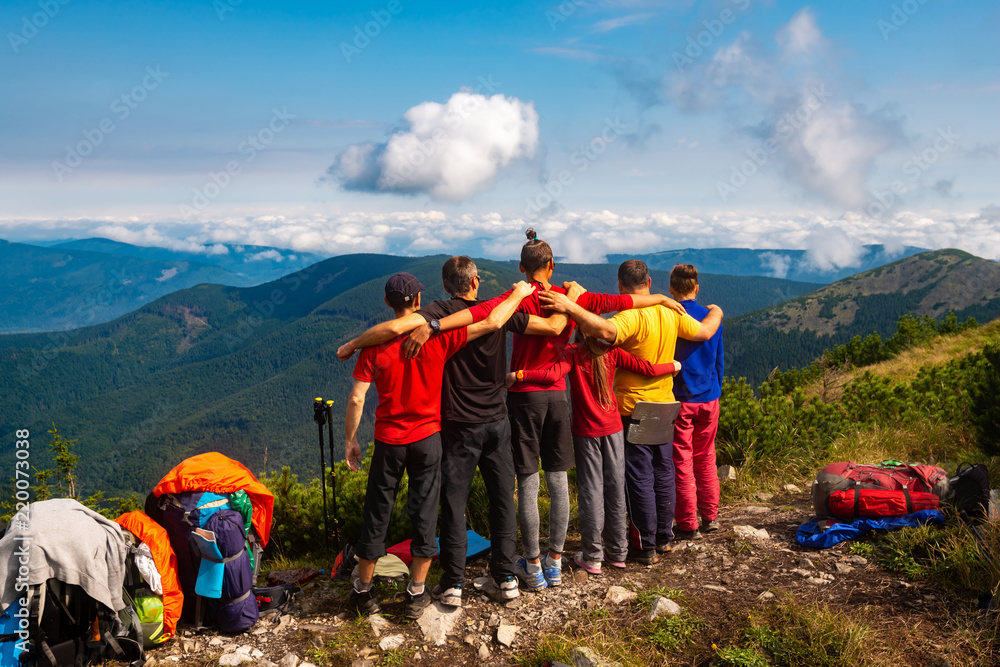 Hikers, friends stand, embracing on a mountain top