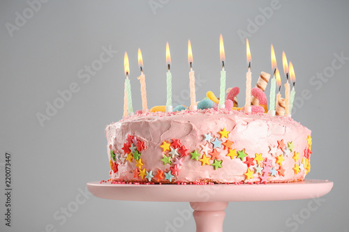 Stand with tasty birthday cake and burning candles on color background