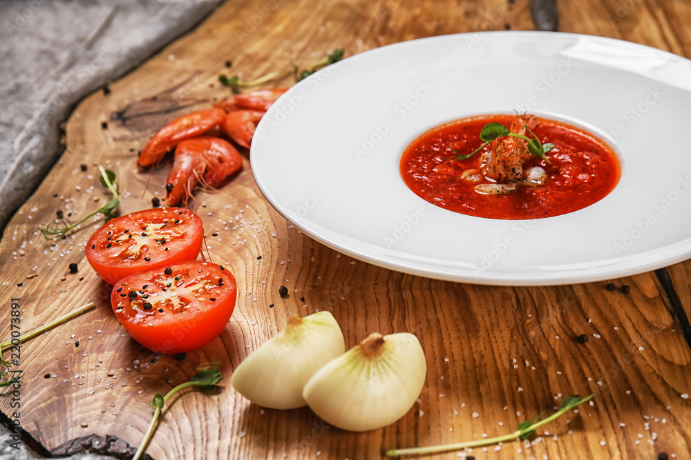 Tasty tomato soup with shrimps in plate on wooden table Tasty tomato soup with shrimps in plate on wooden table