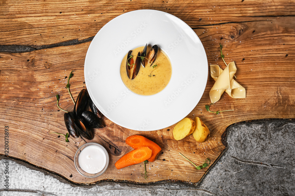 Tasty soup with mussels in plate on wooden table